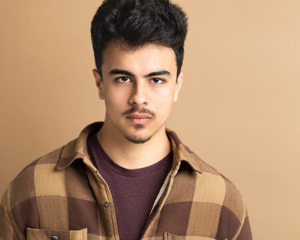 Cyrus Mooney, a head-and-shoulders portrait against a warm tan backdrop, looking toward the camera.